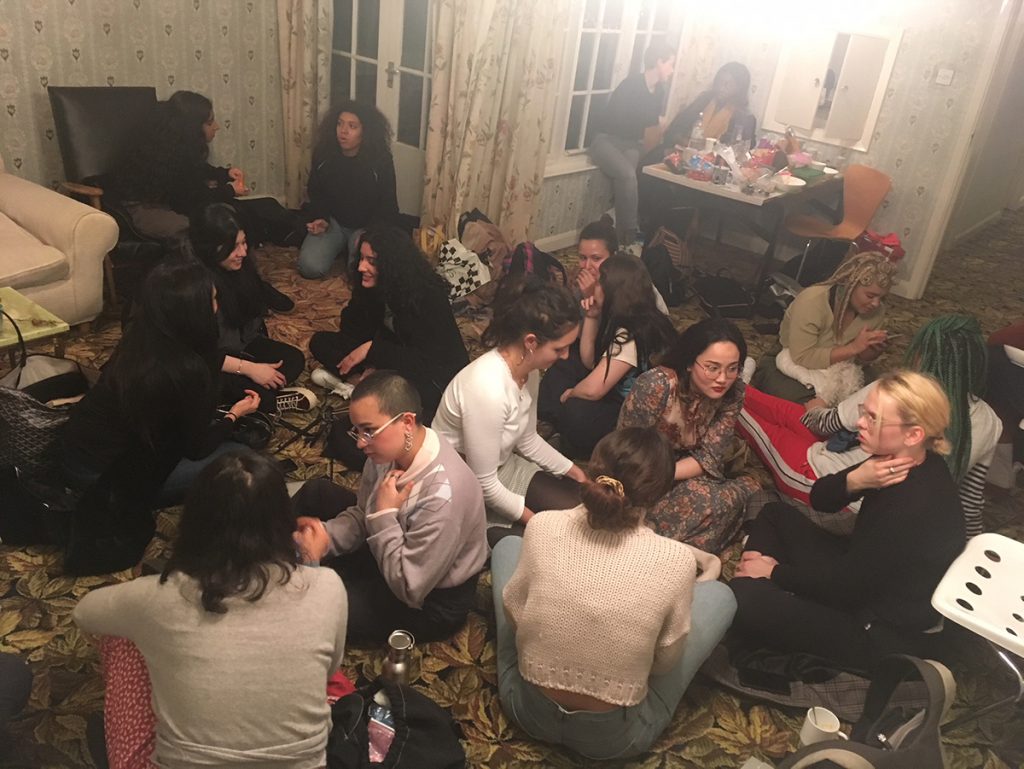 Group of students sitting on the floor of a house chatting in small groups.